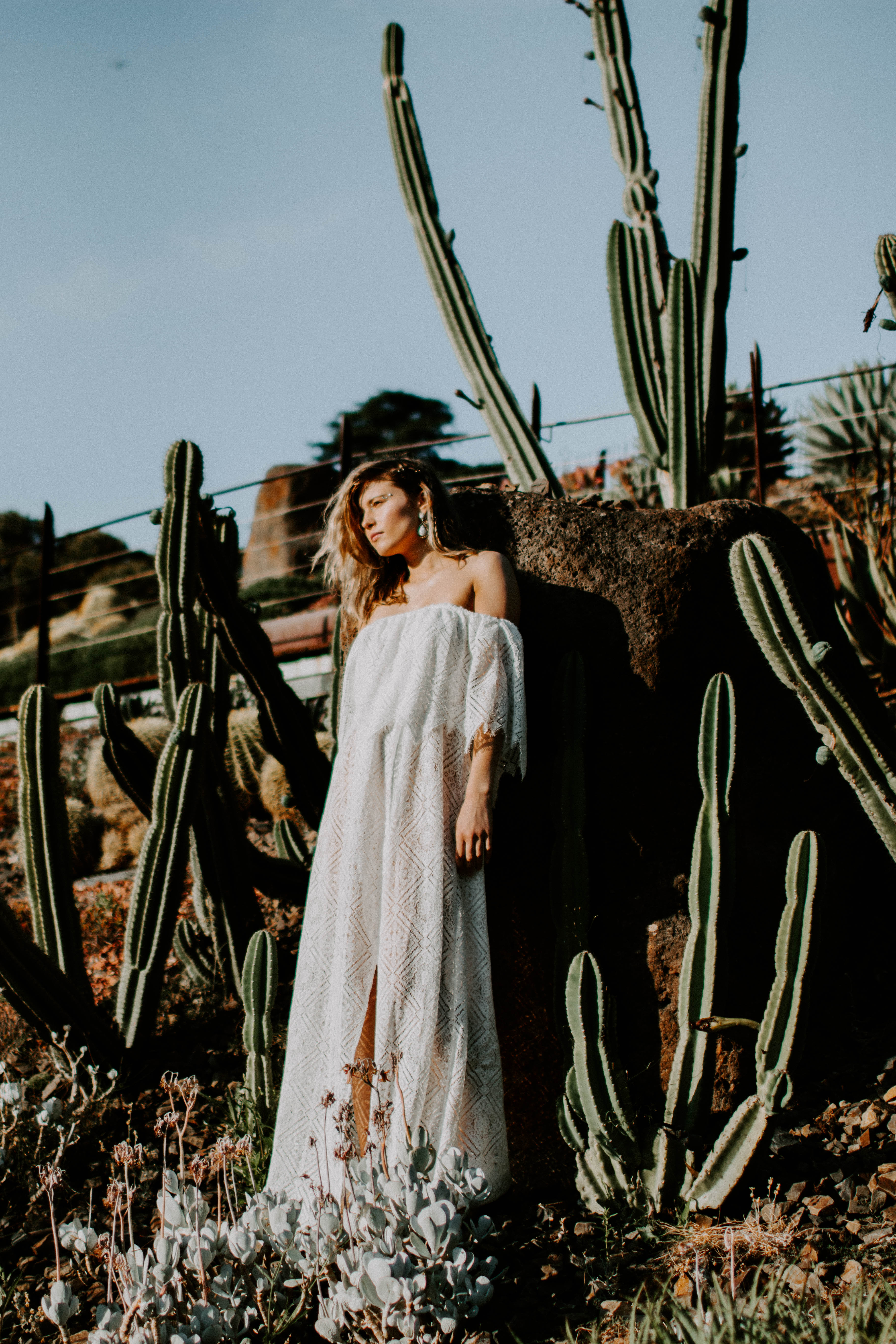 girl wearing bridal dress is standing in a garden of cactus