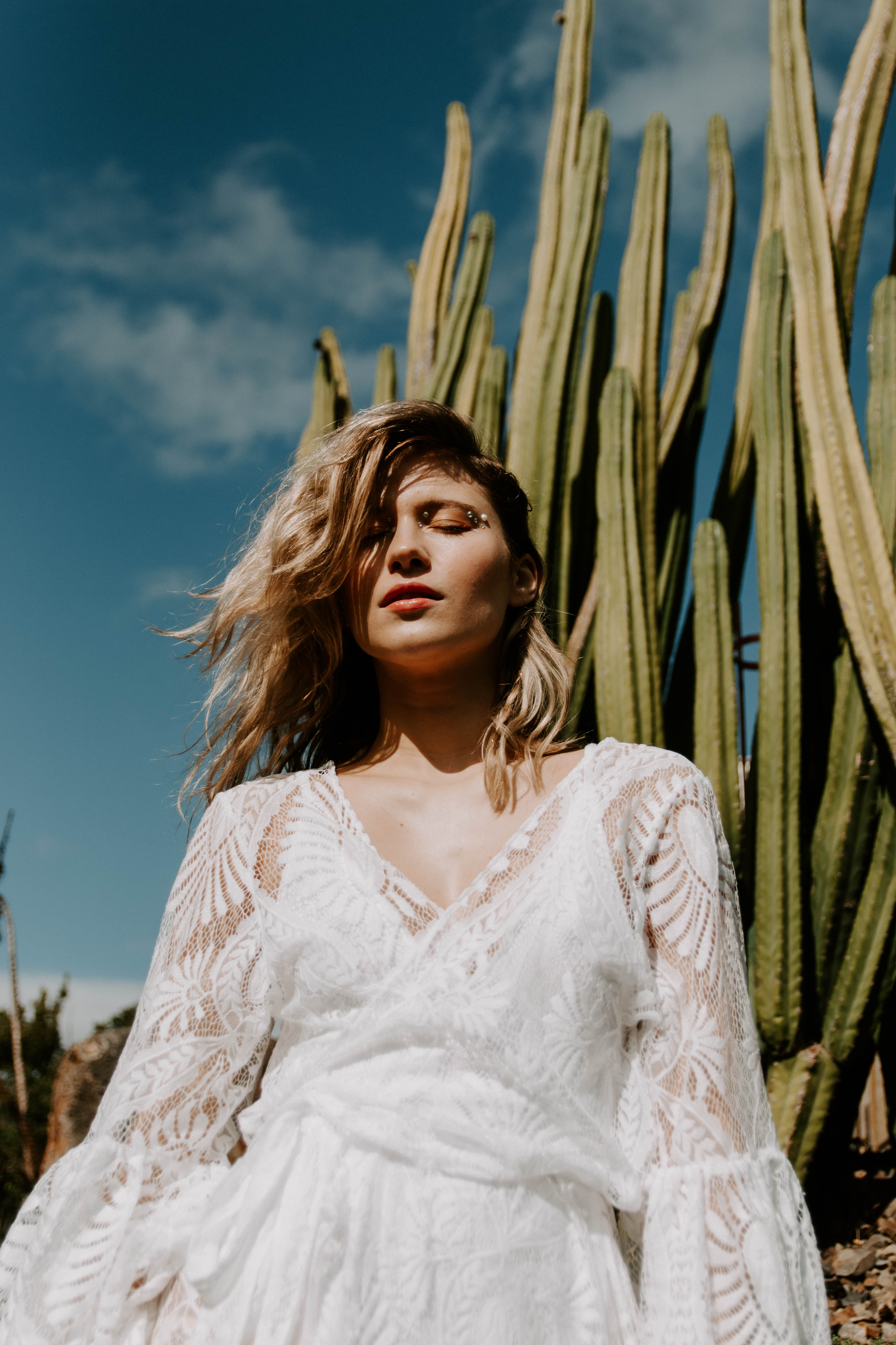 blonde girl wearing lace bohemian dress standing next to cactuses